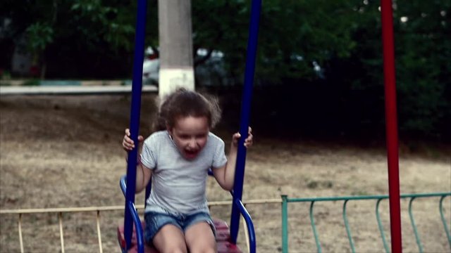 Happy young little girl spinning in a swing and smiling