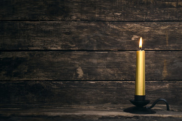 Fototapeta na wymiar Burning candle on aged wooden table background.