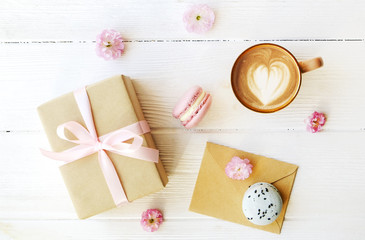 Obraz na płótnie Canvas Blueberry and strawberry flavored french macaron desert cakes, brown cappuccino coffee cup, heart shape latte art, craft paper wrapped present tulip flowers. Isolated background, close up copy space
