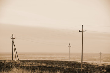 Atmospheric landscape with power lines in field under sky in sepia tones. Background image of electric pillars with copy space. Wires of high voltage above ground. Electricity industry in monochrome.