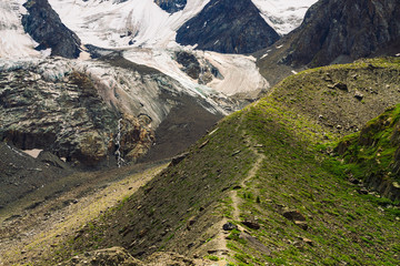 Detailed natural texture of giant mountain covered with snow and ice. Small brooks flow down mountainside. Rock with image of big crying eye. Footpath in highlands. Fantasy artwork of majestic nature.