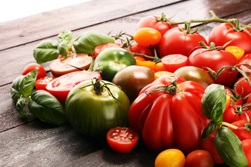 various colorful tomatoes and basil leaves on rustic table.