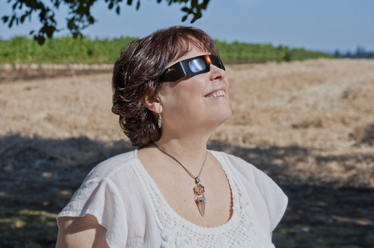 Woman viewing solar eclipse with solar glasses in country field/Woman looking at the solar eclipse with eclipse glasses