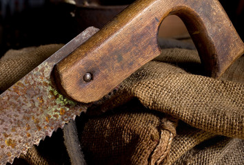 old rusty hand saw with a wooden handle against the background of a vintage canvas bag