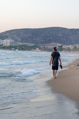 The young man is walking on the beach.