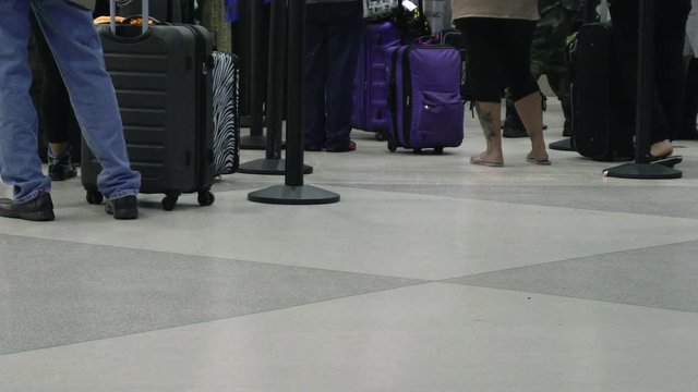 View of peoples legs as they wait in line at an airport terminal, and walk by with their luggage