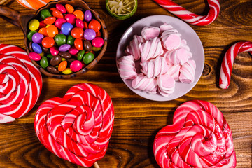 Ceramic plate with marshmallow, candy cane and lollipops on a wooden table. Top view