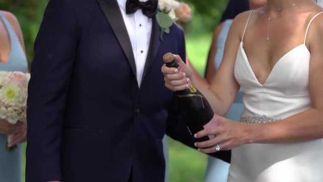 Bride pops champagne with groom outside, in slow motion