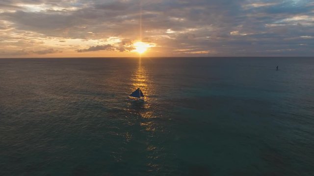 aerial footage sailboat with blue sails at sunset. Sailing yacht on sea surface sunset time.
