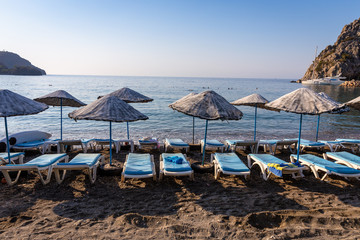 An empty beach in a heavenly bay. Beach umbrellas with sunbeds and towels on towels. Sea and sky...