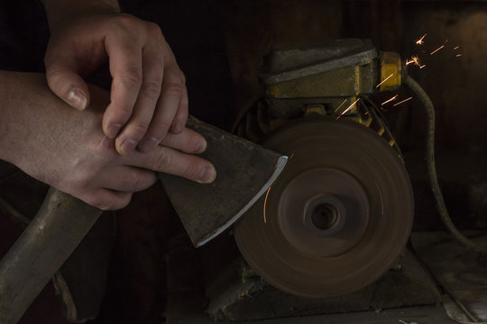 Sharpening the ax in the hands of the man on the grinder. Dark background