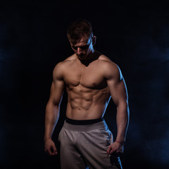 Fitness man on black, posing, with blue smoke on background