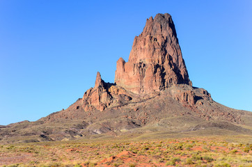 Agathla Peak, a rugged volcanic plug under a perfect blue sky in the landscape near Monument Valley, Arizona