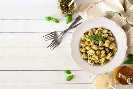 Gnocchi with pesto sauce. Top view table scene over white wood with copy space.