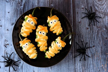 Plate of Halloween mummy jalapeno poppers, top view on with a dark wood background with spiders