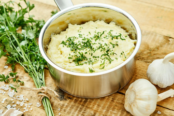 delicious and creamy puree of fresh potatoes sprinkled with parsley in a silver pot on a wooden table