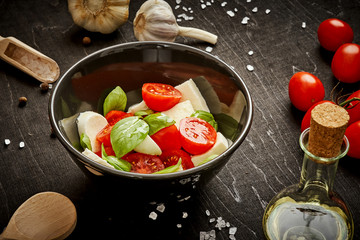 delicious salad with cherry tomatoes mozzarella and basil in a bowl on a black wooden table