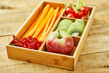 box with delicious carrots, apple, kiwi, cherry tomatoes and redcurrant on a wooden table