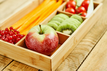 box with delicious carrots, apple, kiwi, cherry tomatoes and redcurrant on a wooden table