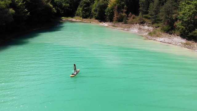 vue a&eacute;rienne sur une jeune femme qui fait du paddle sur un lac vert &eacute;meraude entour&eacute; de for&ecirc;t