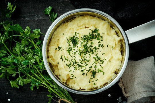 delicious and creamy puree of fresh potatoes sprinkled with parsley in a silver pot on a black table