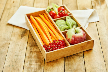 box with delicious carrots, apple, kiwi, cherry tomatoes and redcurrant on a wooden table