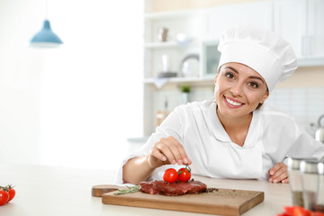 Professional female chef cooking meat on table in kitchen