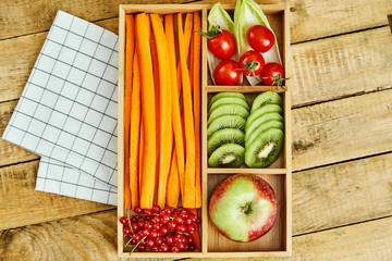 box with delicious carrots, apple, kiwi, cherry tomatoes and redcurrant on a wooden table
