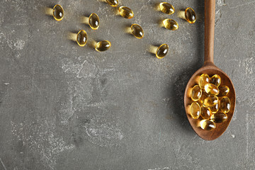 Spoon with cod liver oil pills and space for text on gray background, flat lay