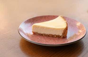 Plate with slice of cheesecake on wooden table