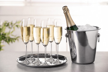 Glasses with champagne and bottle in bucket on table indoors