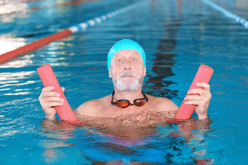 Sportive senior man with swimming noodle in indoor pool