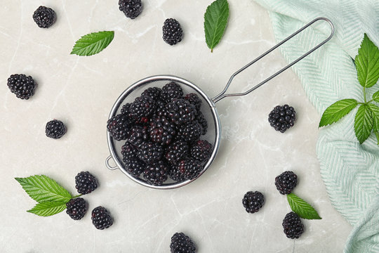 Flat lay composition with strainer of fresh blackberry and leaves on gray background