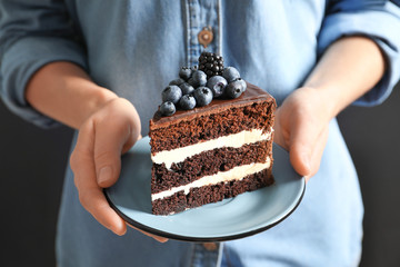 Woman holding plate with slice of chocolate sponge berry cake, closeup