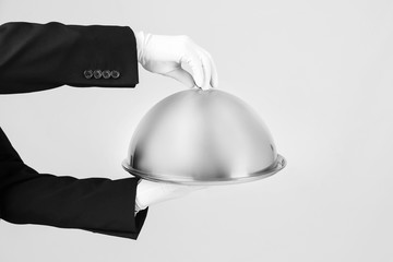 Waiter holding metal tray with lid on light background
