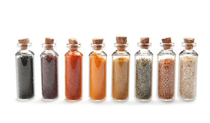 Row of small glass bottles with different spices on white background