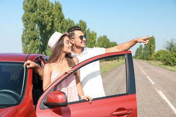 Naklejka premium Happy young couple standing near car on road