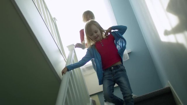 Dutch angle view of two playful little girls of elementary school age running downstairs when spending time together at home, slow motion