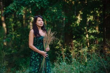 Naklejka premium Beautiful woman standing in the woods with a bouquet of spikelets