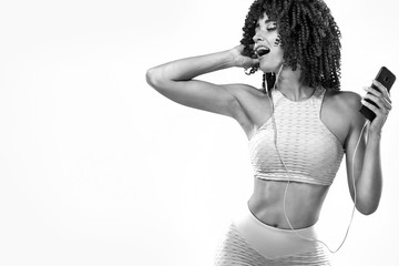 Black and white photo. Beautiful young and fit woman in headphones listening music from phone and smiling. Isolated on a yellow background in a pink sportswear