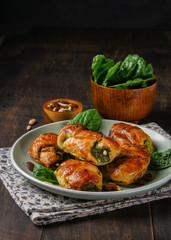 Spinach stuffed croissants with raisins, pine nuts and goat cheese and with a bowl of spinach on the plate with dark background. Space for text, vertical. Healthy concept.