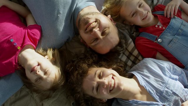 Top view of family with two children of elementary school age lying together on floor or bed and smiling at camera