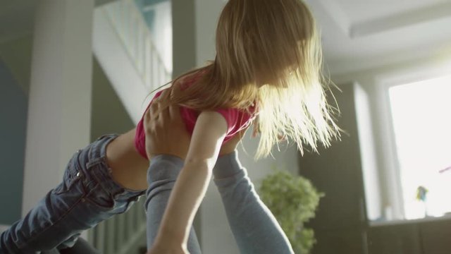 Medium shot of man lying on floor and holding daughter up in the air, girl pretending to be airplane, handheld, slow motion
