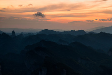 Fototapeta na wymiar Bajiaozhai National Forest Park in Ziyuan County, Guangxi Province China. Dawn, Orange Sunrise, and Danxia Landform Silhouettes. Rugged Mountains, Danxia Cliffs, Candle Peak in the Distance. Abstract