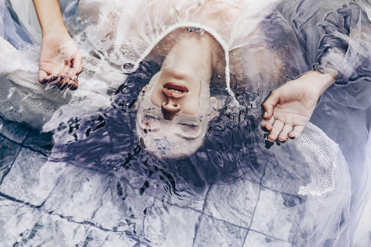 close up portrait of beautiful woman lying on water with fabric. Fashion concept