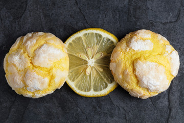 Two cracked crinkle Lemon cookies and slice of fresh lemon on dark background. Close up. Top view.