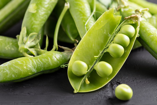 Pods of green peas with leaves on dark background.