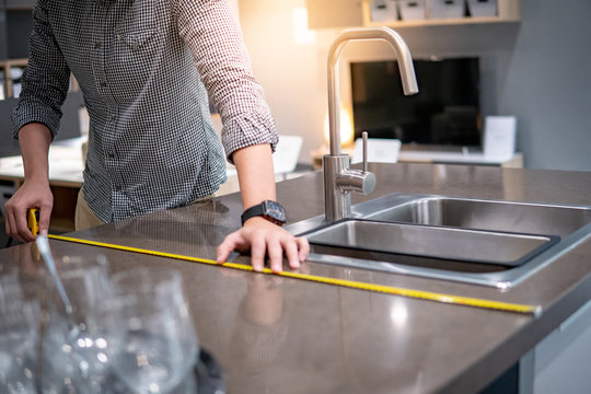 Young Asian Man Using Tape Measure For Measuring Granite Countertops On Modern Kitchen Counter In Showroom. Shopping Furniture For Home Improvement. Interior Design Concept