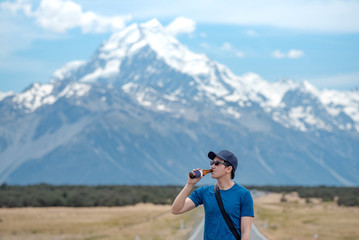 Young Asian male traveler drinking beer at Mount Cook national park, South Island, New Zealand. Road trip travel concept