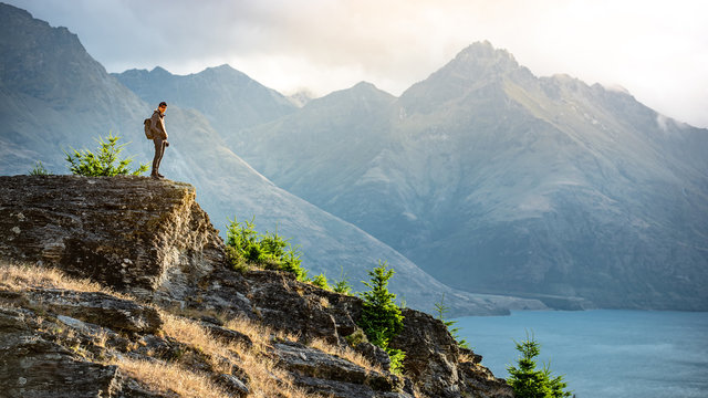 Young male photographer looking at mountain scenery during golden hour sunset in Queenstown, South Island, New Zealand. Travel and photography concept